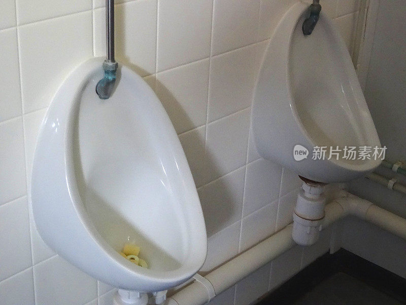 男子公厕/洗手间内的两个白色小便池，墙壁为瓷砖